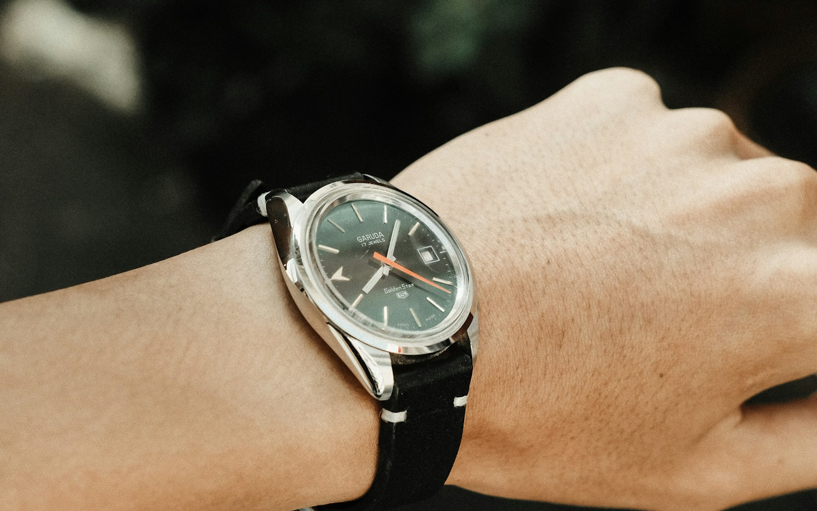 A person winding a mechanical wristwatch beside its instruction booklet